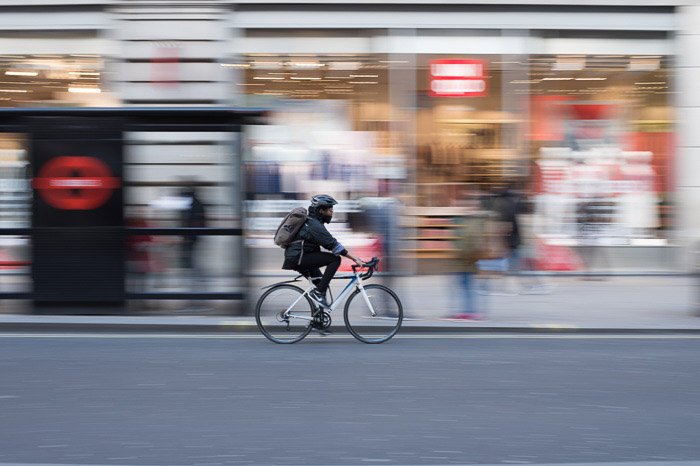 Una persona montando una bicicleta en la ciudad, el fondo es un desenfoque creativo debido al uso de una velocidad de obturación lenta