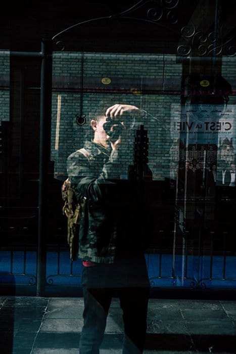 Fotografía de una persona que toma una fotografía reflejada en un escaparate.  Consejos para la fotografía de autorretratos.