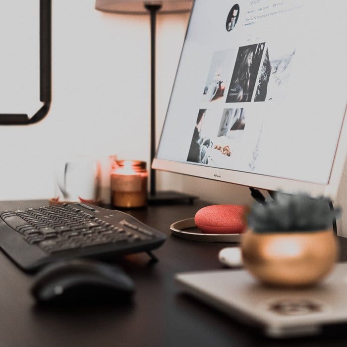 Un escritorio de oficina que contiene una computadora, una planta, una lámpara y otros accesorios.