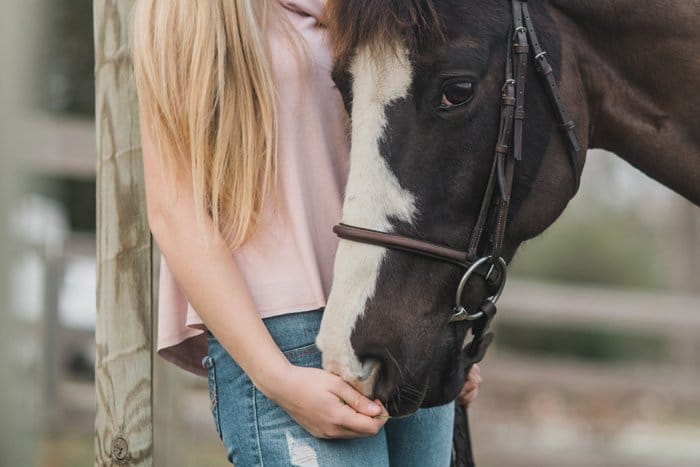 Una chica rubia sosteniendo una brida de caballos. 