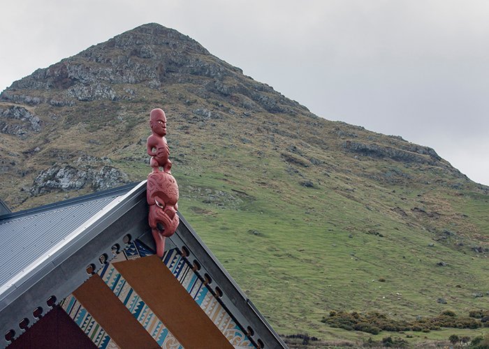 Escultura de talla aborigen roja en una azotea en frente de una montaña 