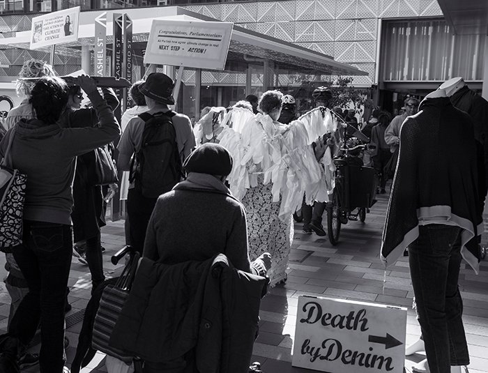 Fotografía en blanco y negro de un grupo de manifestantes frente a edificios y tiendas