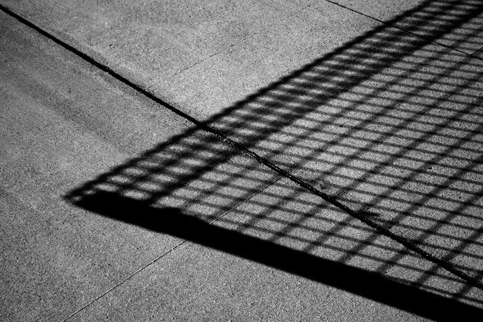 Fotografía en blanco y negro de la sombra de una valla de malla de alambre sobre hormigón.  Ideas de fotografía abstracta.
