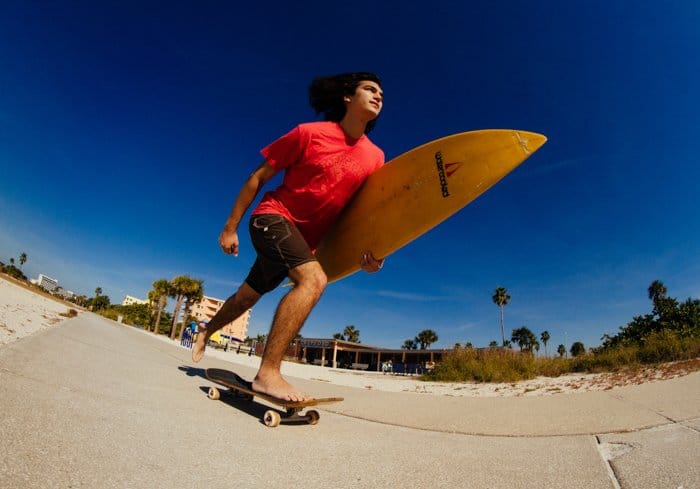 Foto de un chico con una tabla de surf en la mano en una patineta