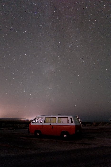 Imagen de una autocaravana roja estacionada bajo un impresionante cielo estrellado. 