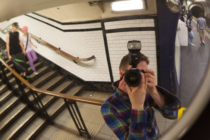 Un fotógrafo tomando un autorretrato en el espejo de una estación de metro, demostrando el uso de tensión dinámica en la composición fotográfica 