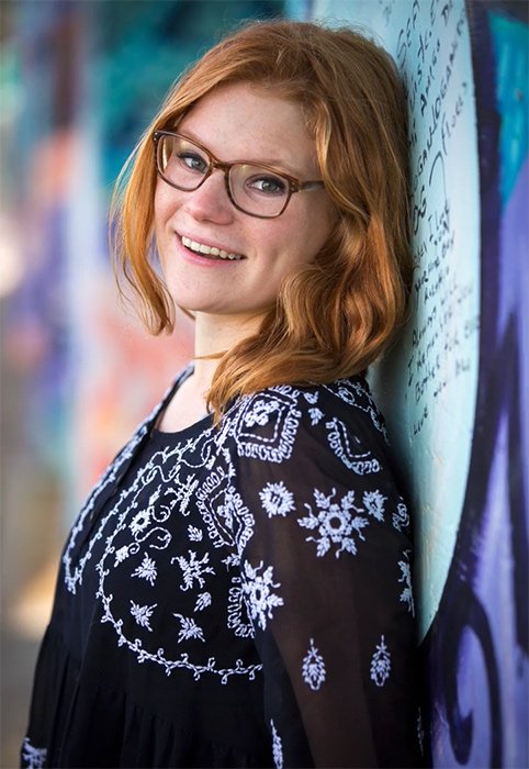 Retrato de una mujer con gafas sonriendo y apoyado contra una pared 