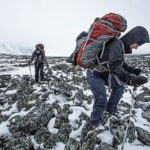 Dos excursionistas con mochilas subiendo una montaña en la nieve.