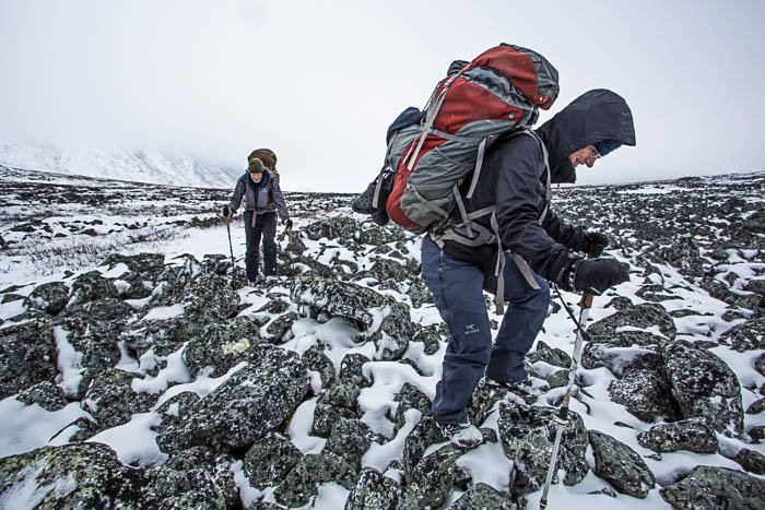 Dos excursionistas con mochilas subiendo una montaña en la nieve.