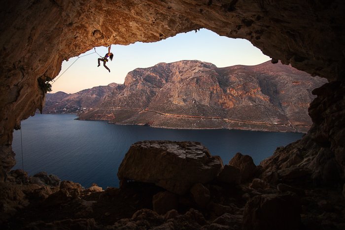 un escalador sobre una cueva junto al agua y un paisaje montañoso: habilidades de fotografía de aventuras