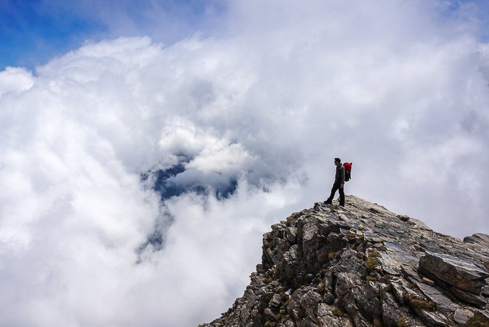 un excursionista de pie en la cima rocosa de un paisaje montañoso: habilidades de fotografía de aventuras
