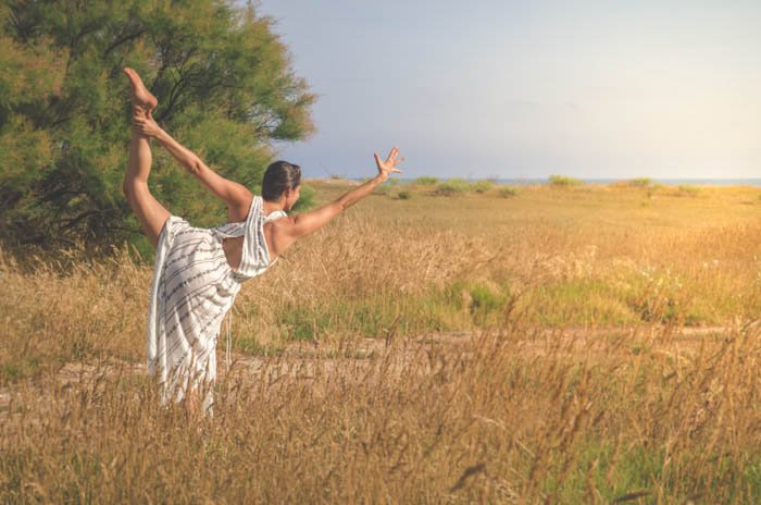 Chica con un vestido blanco realizando la pose de bailarina en un campo de trigo