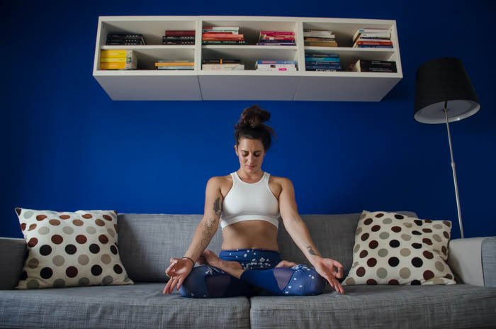 Fotografía de yoga creativa que muestra un modelo femenino en posición de loto en un sofá gris