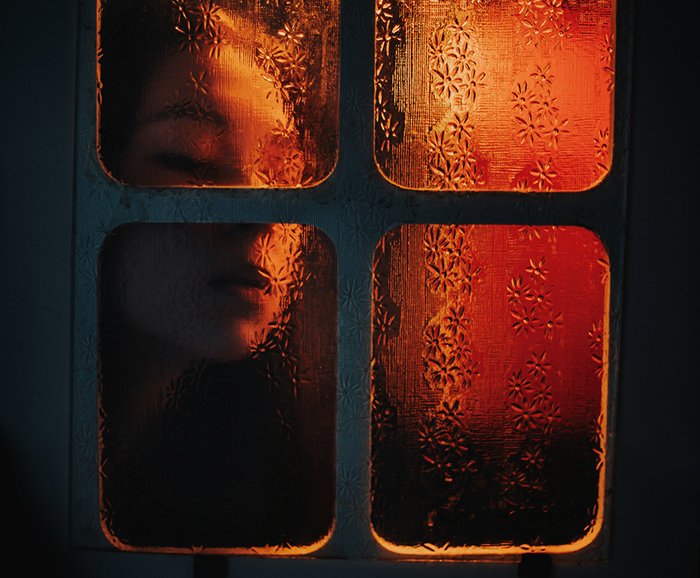 Retrato atmosférico de una niña con la cara presionada contra el cristal de una ventana con iluminación ambiental