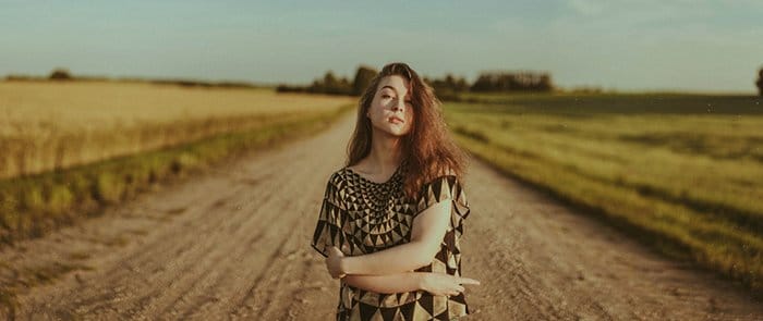Hermoso retrato de cerca de una mujer posando en una carretera rural rodada con luz ambiental