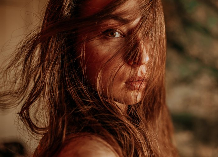 Hermoso retrato de cerca de una niña con el pelo que cubre su rostro, filmado con iluminación ambiental para un efecto de ensueño