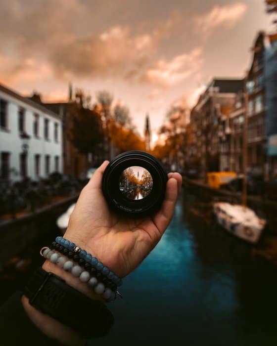 Fotografía creativa de una persona sosteniendo una lente de cámara delante de la cámara en Groenburgwal, Amsterdam