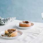 Dos platos de tartas de pera y almendras sobre una mesa blanca junto a una copa de vino tinto