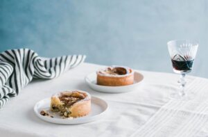 Dos platos de tartas de pera y almendras sobre una mesa blanca junto a una copa de vino tinto