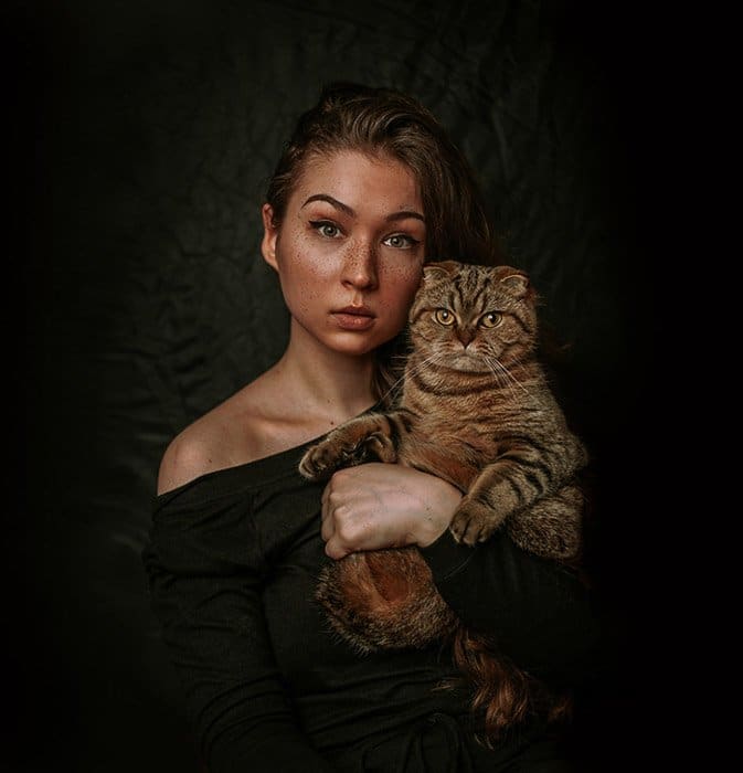 Retrato atmosférico de un modelo femenino sosteniendo un gato marrón 
