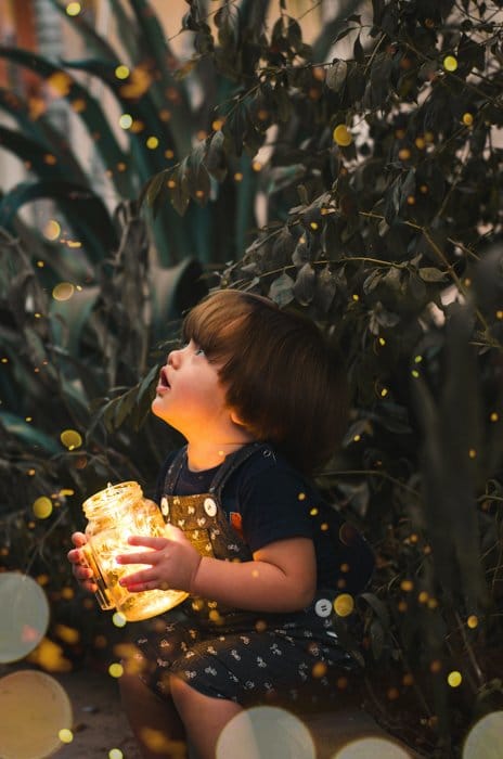Una fotografía infantil mágica de un niño rodeado de luces bokeh de hadas.