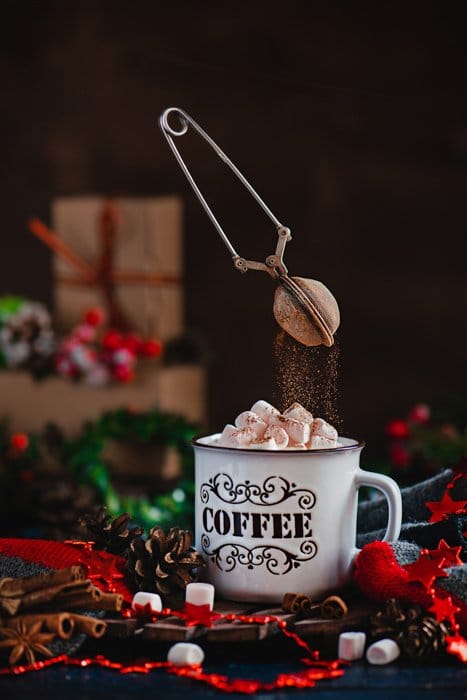 Una mágica fotografía navideña de una taza de café con malvaviscos y un rociador de chocolate levitando