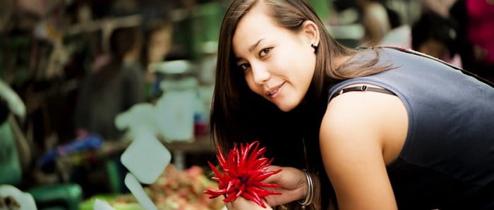 Un retrato de aspecto cinematográfico alegre de una modelo femenina posando con chiles rojos en un mercado