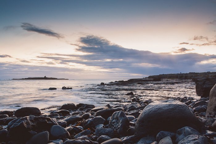 Foto de mirador bajo de rocas en la costa al amanecer contra un amanecer nublado y suave iluminado