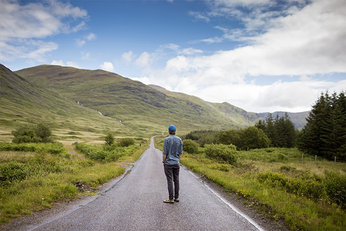 Una imagen de paisaje con un hombre parado en medio de una carretera rural.