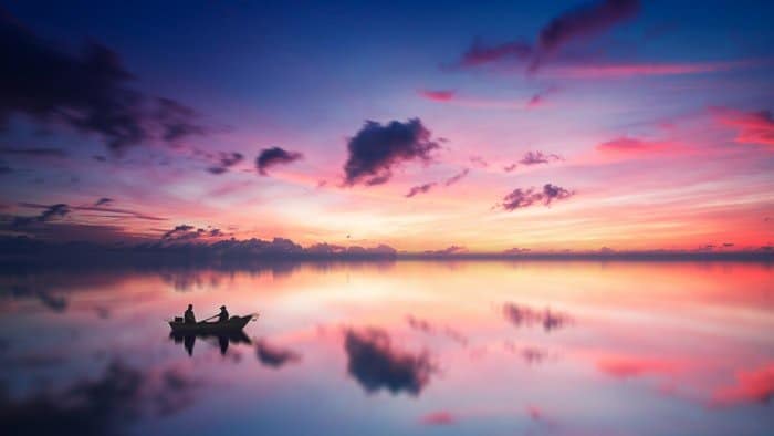 Nubes de colores sobre un lago con la silueta de un barco