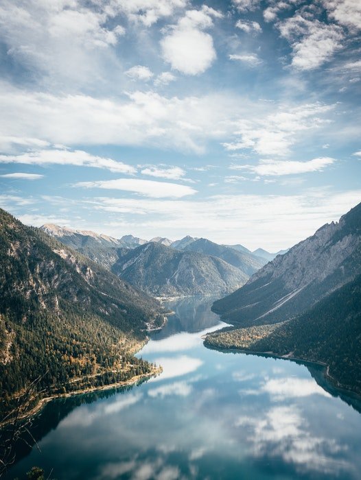 Una foto de paisaje de un río que atraviesa una cadena montañosa con nubes y cielo arriba