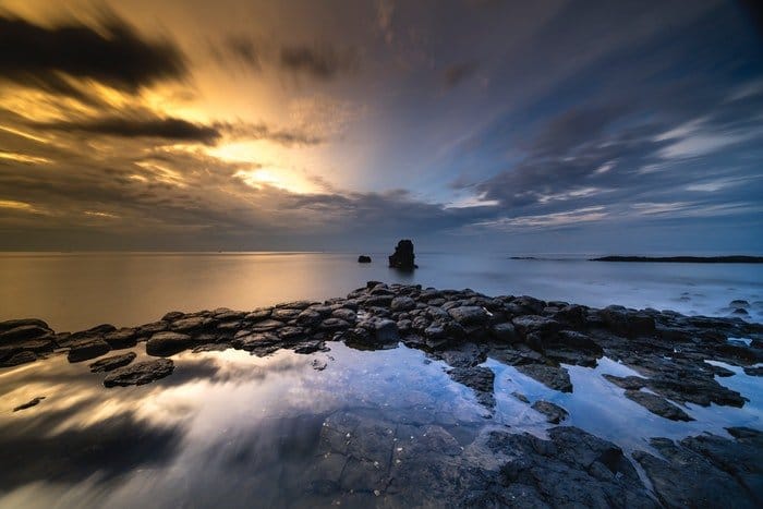 Una fotografía de larga exposición de nubes sobre el agua y rocas.