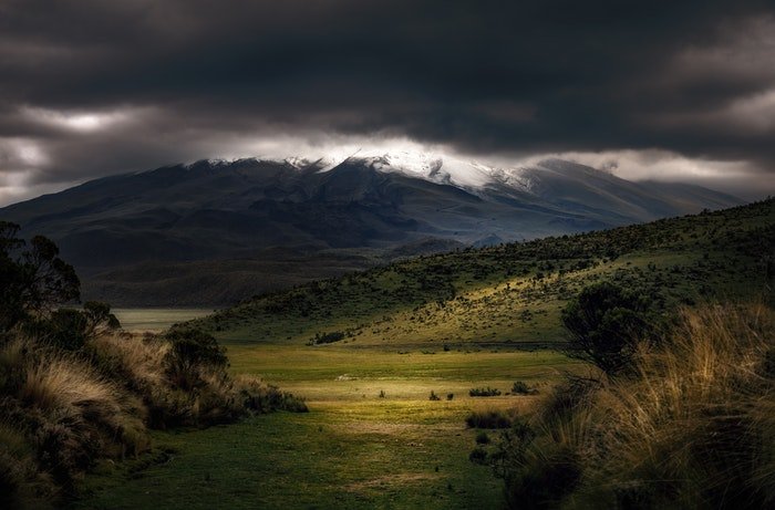 una imagen de un valle con nubes oscuras arriba y un charco de luz en primer plano