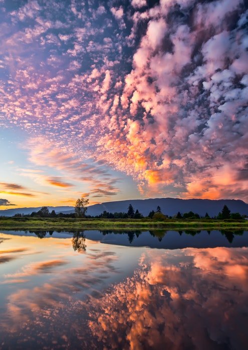 Una fotografía de nubes arriba reflejadas en un lago abajo con tonos rosados.