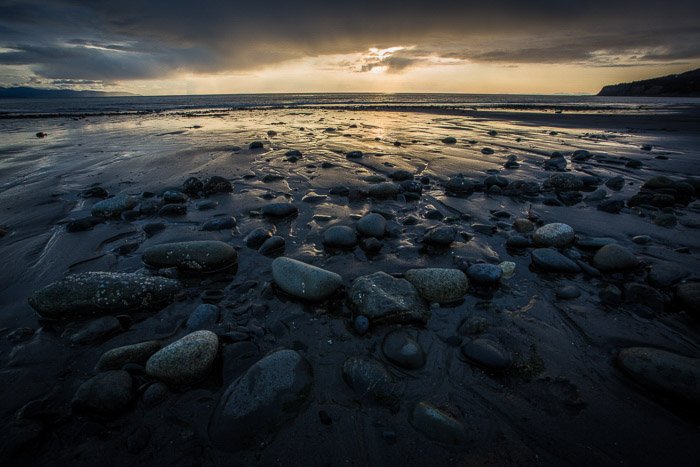 Fotografía costera: rocas de color oscuro en aguas poco profundas al anochecer