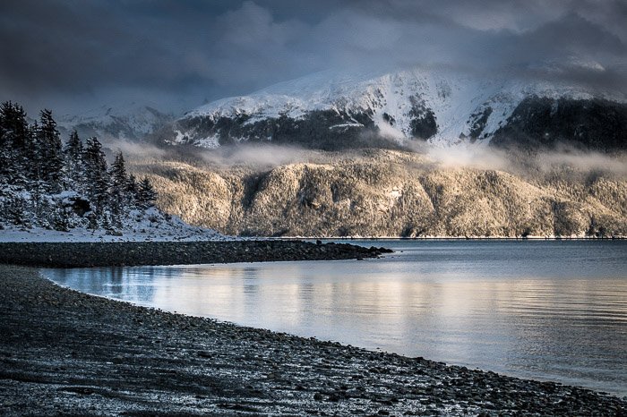 Fotografía costera: costa rocosa con montañas nevadas de fondo