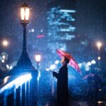 Foto de una mujer de pie bajo un paraguas en la nieve con luces azules en el fondo