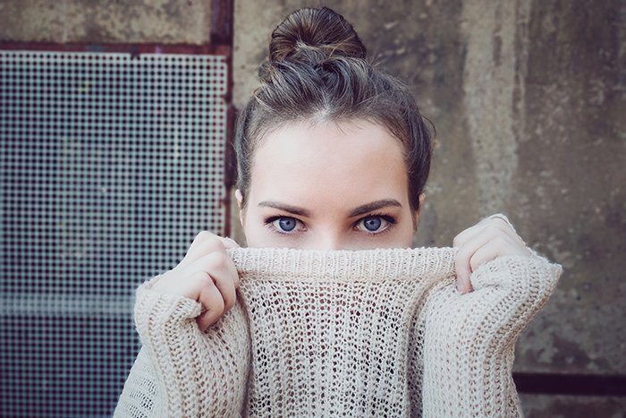 Foto de retrato de una mujer con ojos azules tirando de su suéter delante de su boca