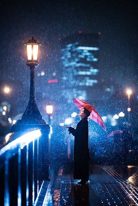 Foto de una mujer de pie bajo un paraguas en la nieve con luces azules en el fondo