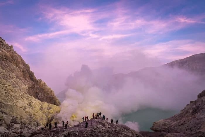 Foto de personas de pie sobre un acantilado con el hermoso cielo púrpura arriba