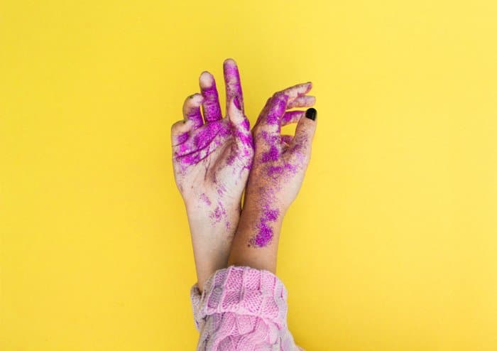 Una imagen divertida de manos cubiertas de pintura y brillo con un fuerte uso de colores complementarios amarillo y morado. 