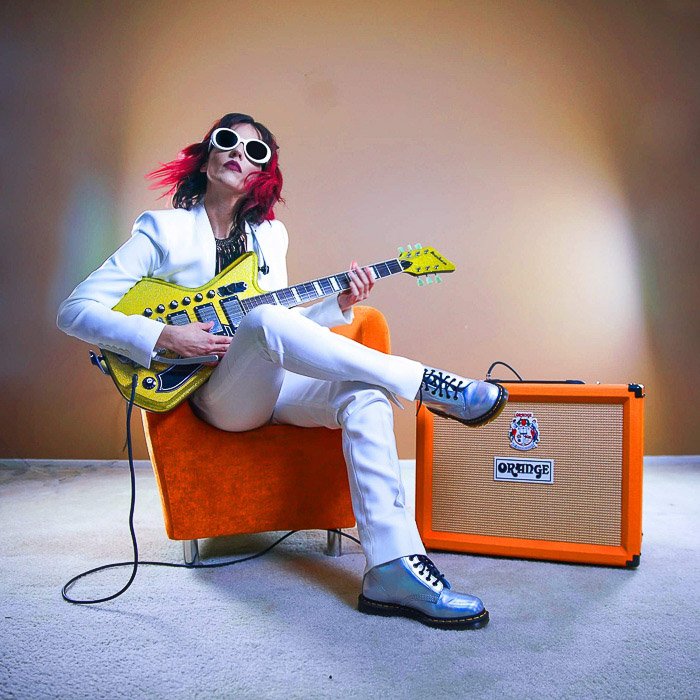 Una niña tocando la guitarra eléctrica con amplificador naranja