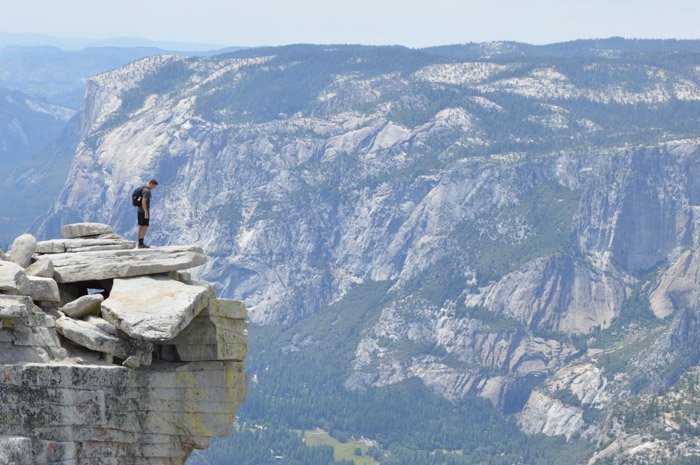 Un hombre de pie al borde de un acantilado con un impresionante paisaje montañoso detrás de él, demostrando el equilibrio de tamaño y peso en la fotografía