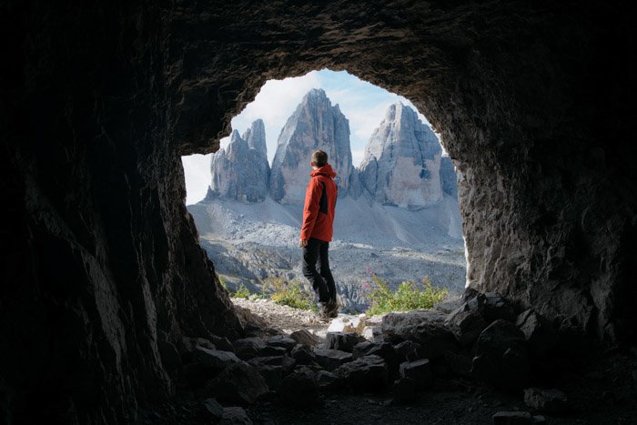 Un excursionista natural enmarcado por una cueva en primer plano. 