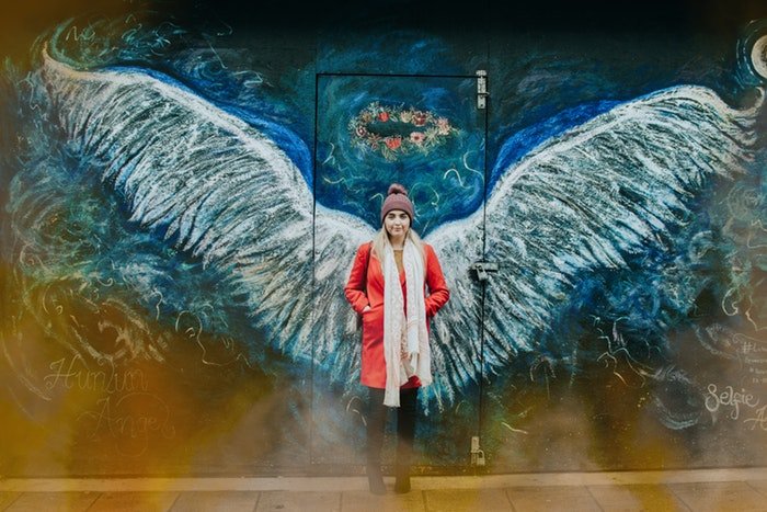Mujer de pie delante de la pared con alas de ángel dibujadas en él 