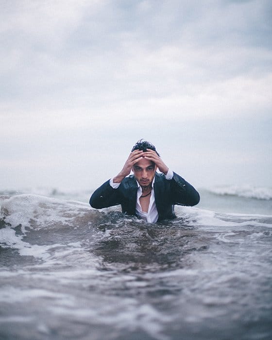 Un dramático retrato conceptual de un hombre que emerge del mar con las manos en la cabeza - ideas de fotografía conceptual