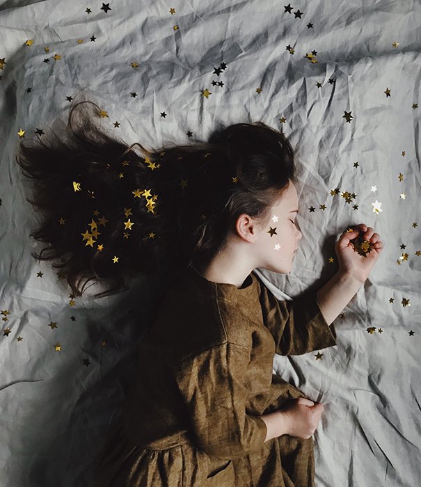 Un retrato conceptual de ensueño de una niña durmiendo, cubierta de estrellas doradas