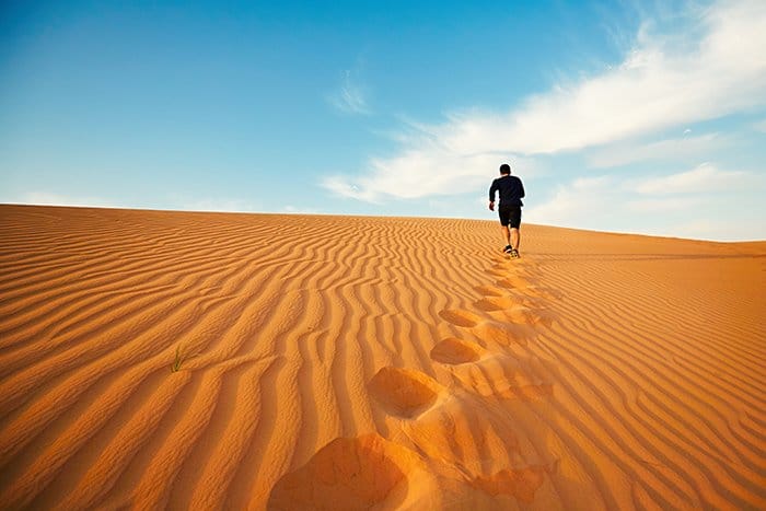 El hombre joven corre a la cima de la duna en el desierto.