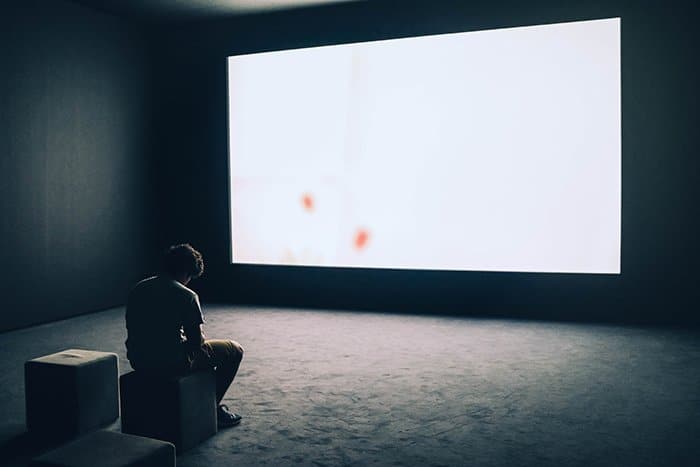 Un autorretrato conceptual de un hombre sentado frente a una gran pantalla en blanco