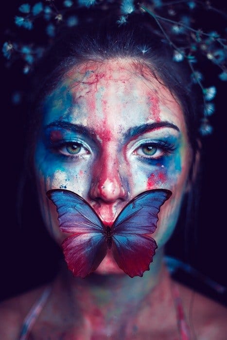 Mujer con la cara pintada y una mariposa en la boca 